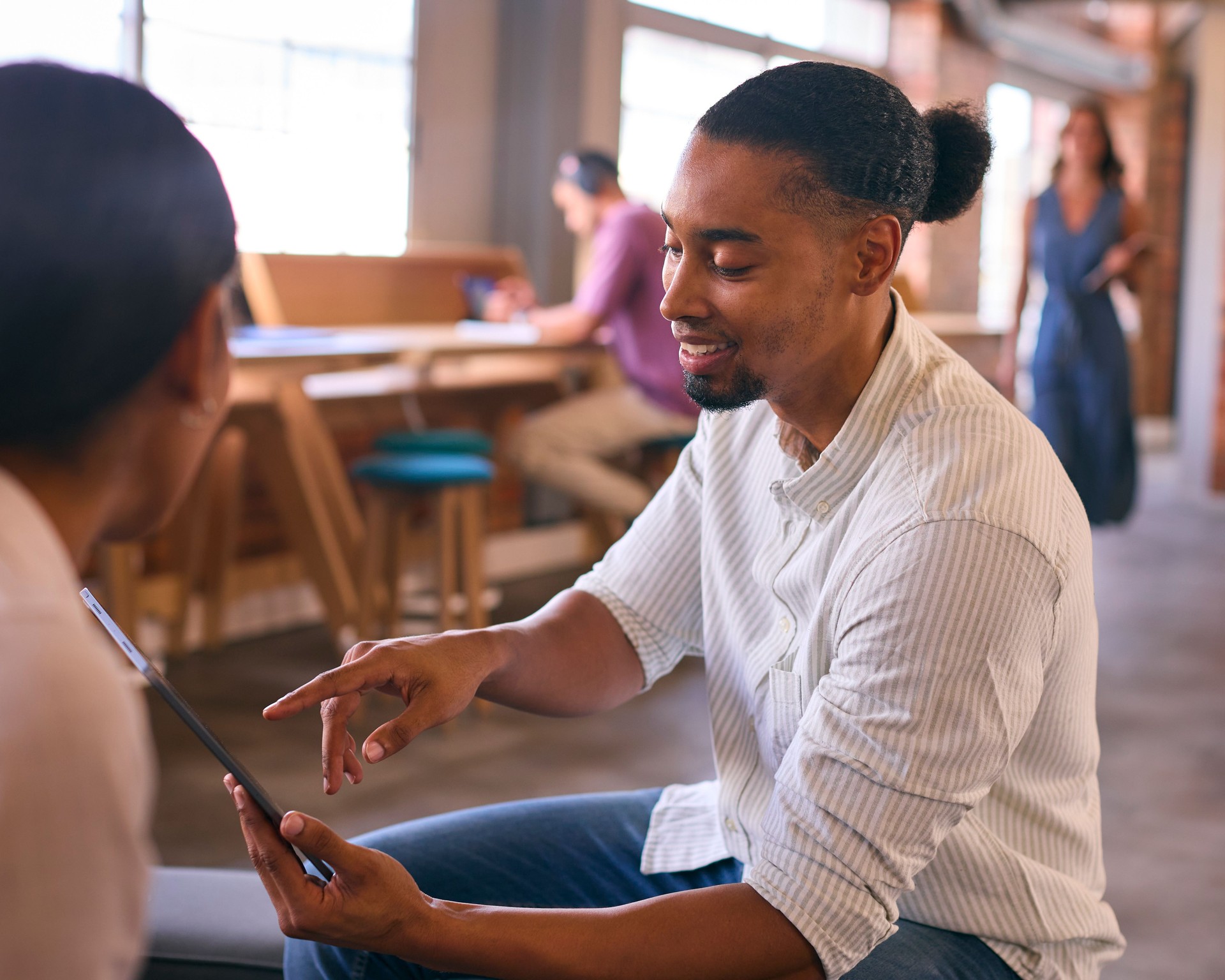 Two Young Businesspeople With Digital Tablet Meeting In Office With Colleagues In Background Two Young Businesspeople With Digital Tablet Meeting In Office With Colleagues In Background